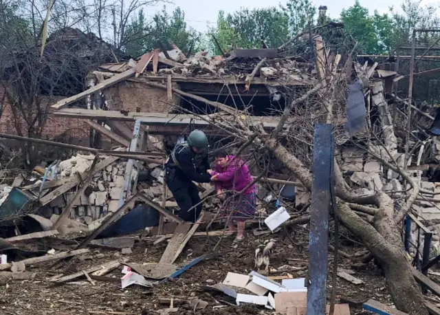 A police officer helps a woman to evacuate a destroyed building in Kostiantynivka