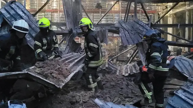 Firefighters walk through the wreckage of a destroyed warehouse