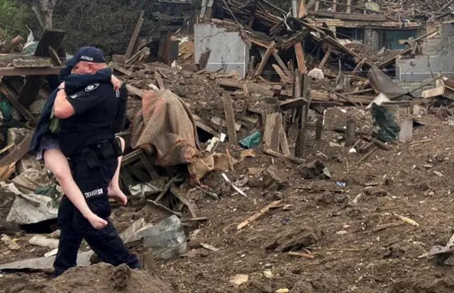 A police officer carries a child away from a destroyed house in Kramatorsk