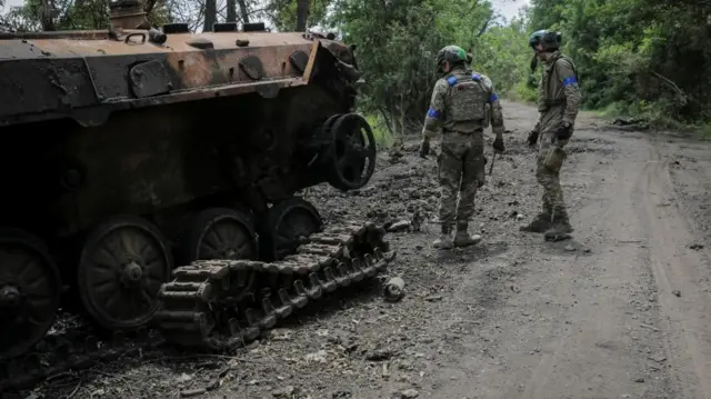 Two Ukrainian servicemen inspect a destroyed vehicle