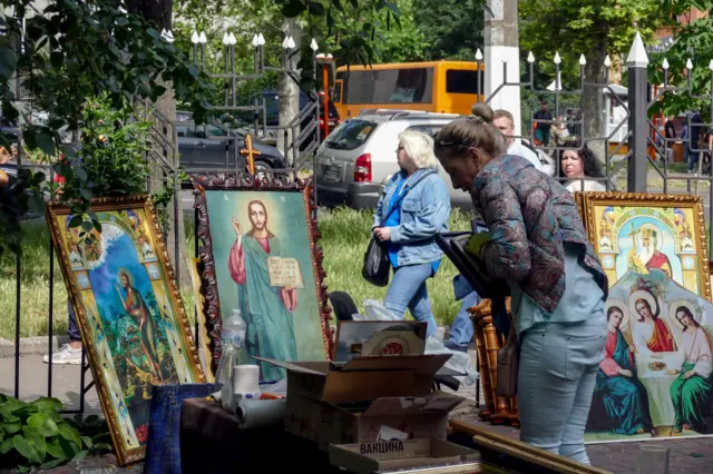 A woman cleans religious icons near a damaged church after a missile strike in Odesa