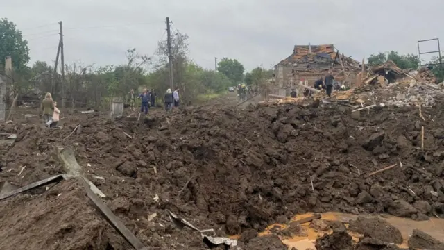 Civilians stand next to a huge crater