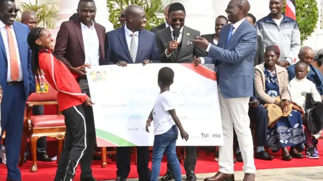 Faith Kipyegon (L) receiving the giant cheque from William Ruto (R)