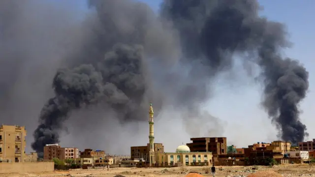 A man walks while smoke rises above buildings after aerial bombardment, during clashes between the paramilitary Rapid Support Forces and the army in Khartoum North,