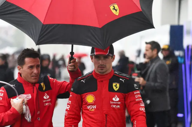 Charles Leclerc walks under an umbrella in the paddock in Canada