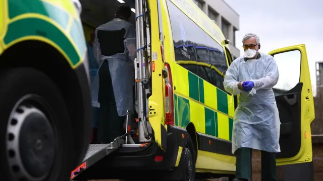 A paramedic wearing personal protective equipment (PPE) exits an ambulance