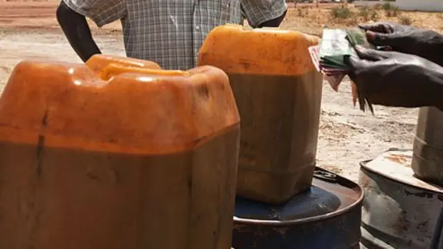 People exchange cash for jerry cans of petrol.