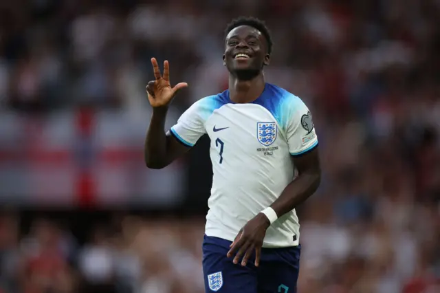 England's Bukayo Saka smiles and puts up three fingers after scoring a hat-trick