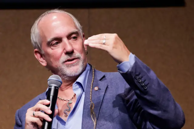 Richard Garriott appearing with a microphone. He has a snake necklace.