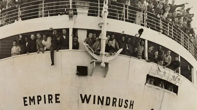 Front of a ship with crowds of people hanging over railings