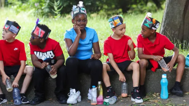 Children wear headdresses with flags and feathers as part of a procession