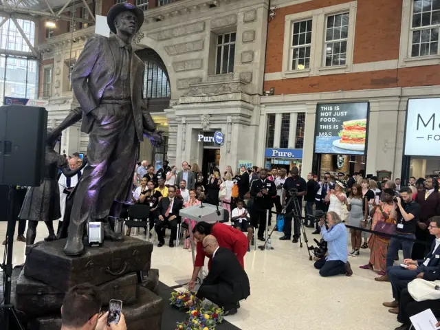 People lay wreaths at the base of the Windrush statue in London's Waterloo station