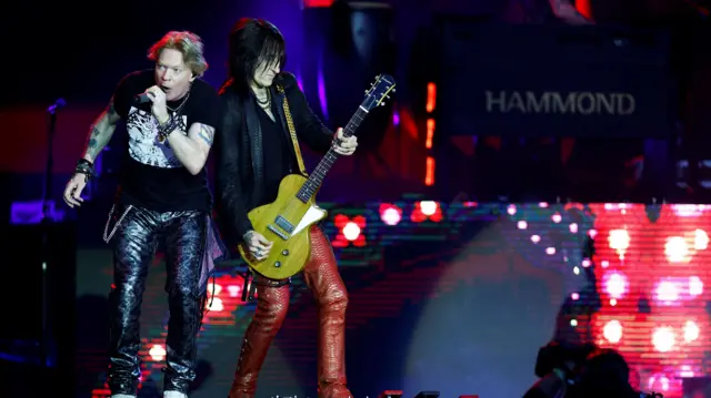 Axl Rose and Richard Fortus leaning against each other on stage