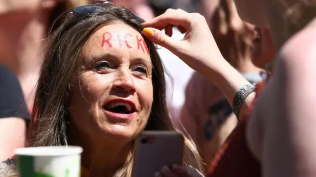 A fan waits for Rick Astley’s Glastonbury set with the word “RICK” written in red across her forehead