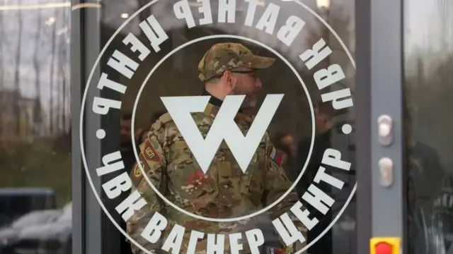 A soldier stands in front of a Wagner emblem