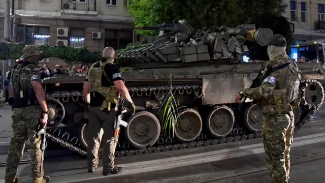 Three Wagner Group servicemen stand next to tank in Rostov-on-Don,