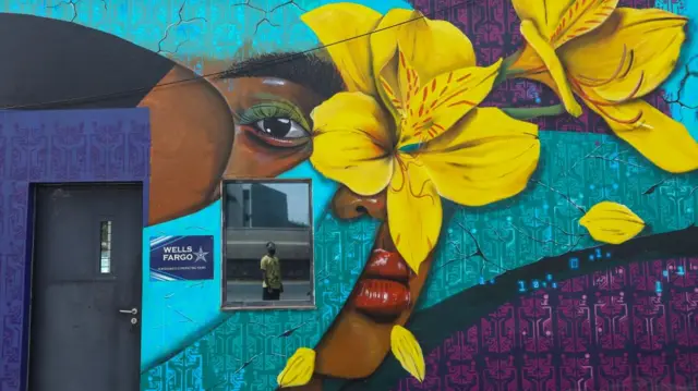 Kenyan graffiti artist Bhupi Jethwa (C), popularly known by his stage name WiseTwo, is relfected in a window mirror next to one of his murals on a roadside wall in Nairobi