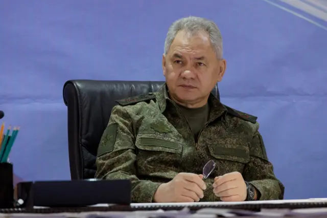 Sergei Shoigu sits at a desk in military fatigues