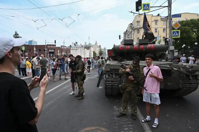 A man takes a picture of another man standing with Wagner fighter in front of a tank