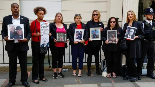 Family members and partners of people who died during the pandemic hold pictures of their loved ones outside the inquiry