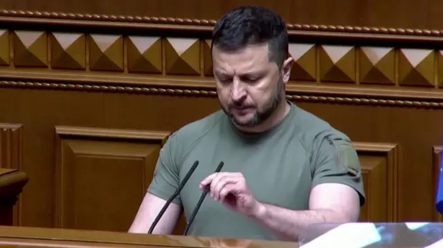 President Zelensky adjusts a microphone before speaking to Ukraine's parliament