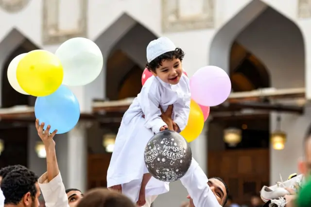 A boy being lifted aloft by balloons on Eid al-Adha at the historic Azhar mosque in the centre of Cairo - 28 June 2023