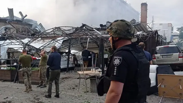 Ukrainian rescuers and policemen work on the site of a rocket hit in downtown Kramatorsk