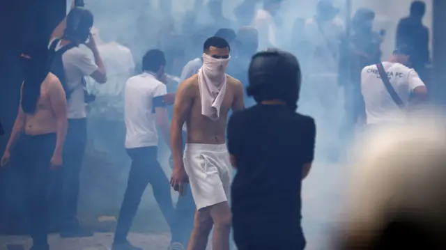 Masked protesters walk amid tear gas during clashes at a march in Nanterre