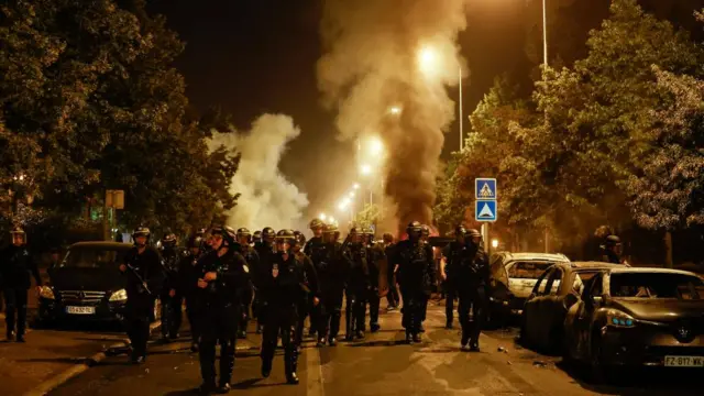 Riot police walk near burnt cars during clashes with protesters in Nanterre