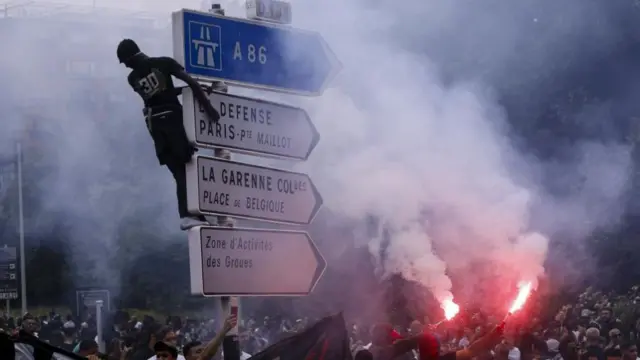 Protesters in Nanterre burning flares and one man has climbed a road sign