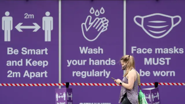 Masked person walking past covid posters in Glasgow