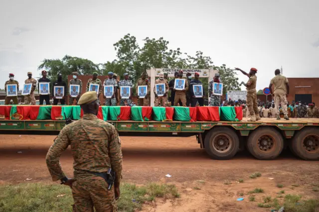 Burkina Faso's servicemen holds soldiers' portraits behind the coffins during the burial of the soldiers killed in Gaskinde, in Ouagadougou on October 8, 2022.