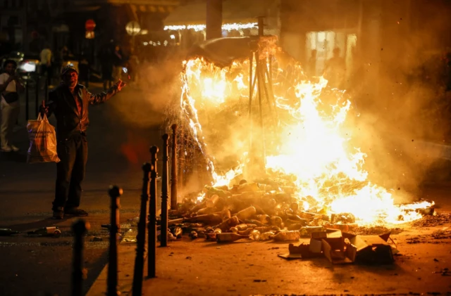 A man gestures next to a burning container as people protest following the death of Nahel, a 17-year-old teenager killed by a French police officer in Nanterre during a traffic stop, and against police violence, in Paris