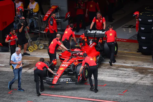 Charles Leclerc's Ferrari is pushed back into the garage by mechanics