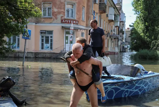 Man carries woman on his back through flooded Kherson