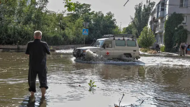 Red Cross volunteers drive a car on a flooded street after the Nova Kakhovka dam breached, in Kherson