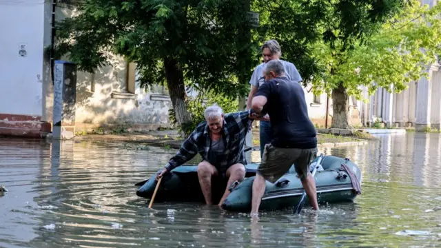 People help an elderly man to get in an inflatable boat as he evacuates from his home in a flooded street of Kherson