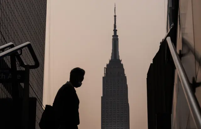 The Empire State Building stands in the background as a person wearing a mask walks on a hazy Wednesday morning