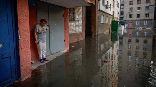 A woman stands next to the entrance to her home on a flooded street in Kherson after the Nova Kakhovka dam breached