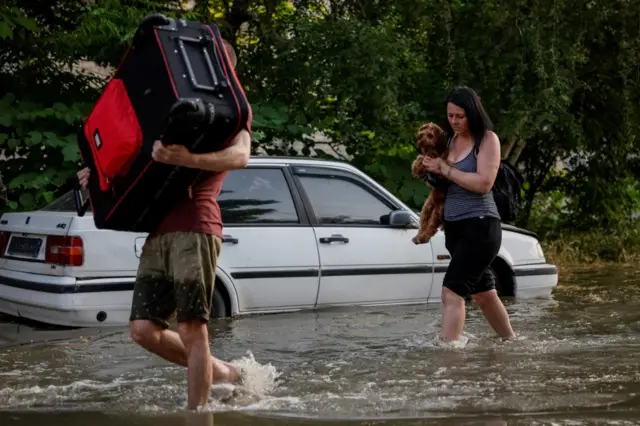 Local Kherson residents carry their personal belongings on a flooded street