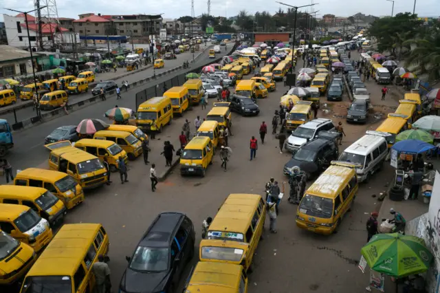 Commuters walk next to parked public transport mini buses at Ojodu Berger bus station in Lagos, on June 1, 2023.