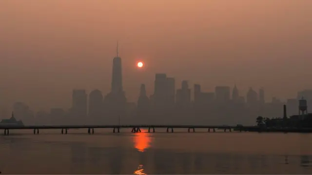 An orange sun hangs over the city skyline of New York.