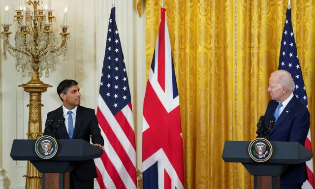 Sunak and Biden look at each other in front of UK and US flags at a press conference