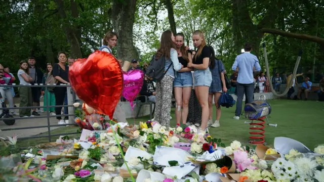 A girl is comforted by friends as she cries at the side of the growing site of tributes