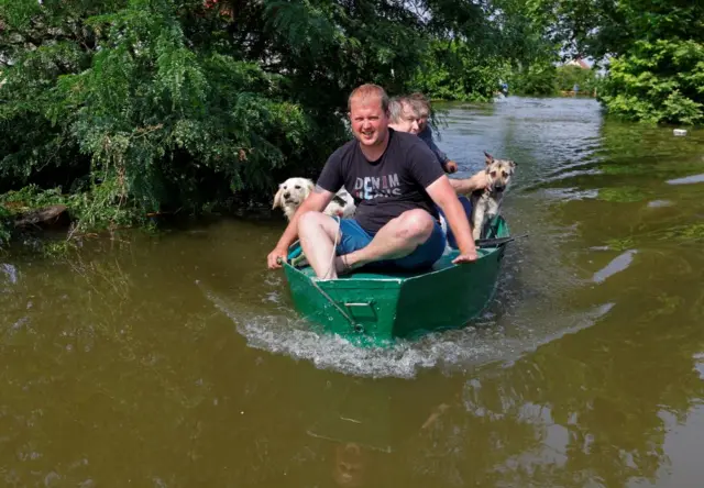 People sail in a boat in the flooded town of Hola Prystan, Kherson