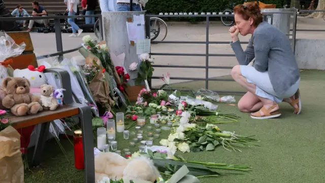 A woman cries as she kneels before the flowers and tributes left at Le Paquier park