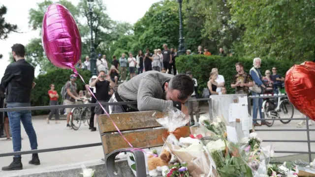 A man cries with his head in his hands on the bench where tributes have been laid