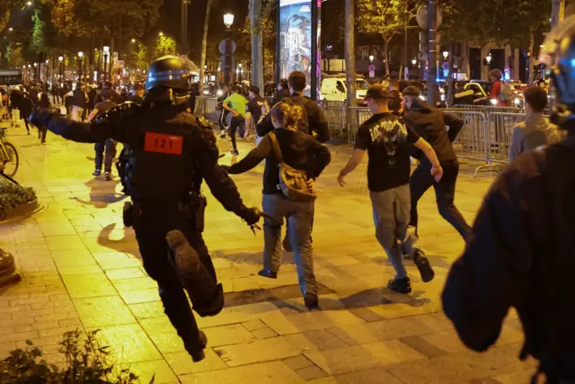 People run followed by police officers on the Champs Elysees in Paris