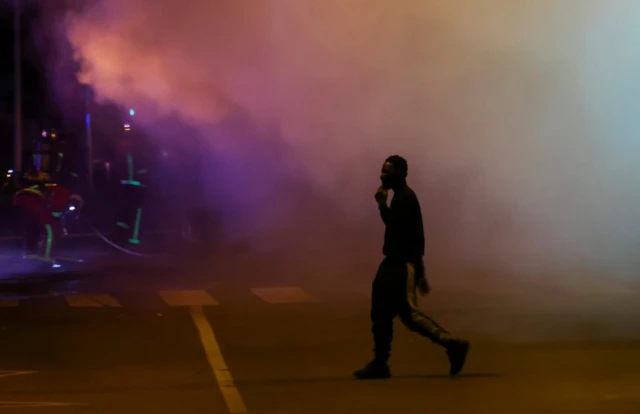 A person walks while firefighters work as unrest continues in Nanterre, Paris