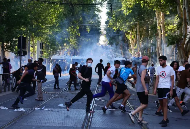 Protesters run from launched tear gas canisters during clashes with police in Marseille, southern France, on 1 July 2023